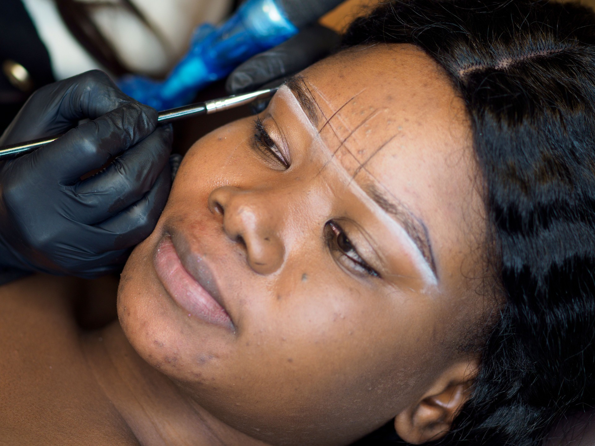 Beautician drawing correction lines for eyebrow permanent tattoo young african woman, beauty saloon