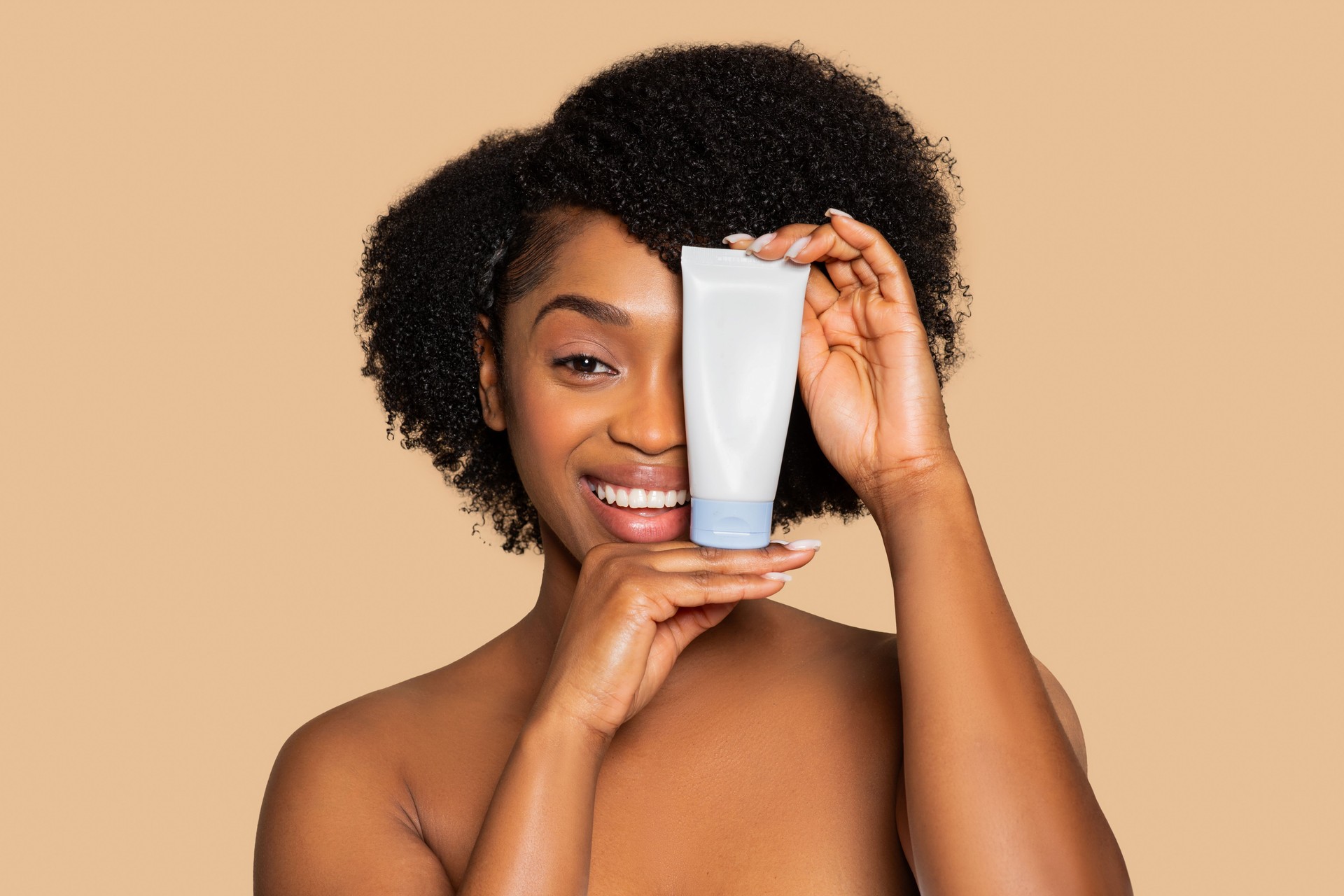 Smiling black woman holding skincare tube beside her face, mockup